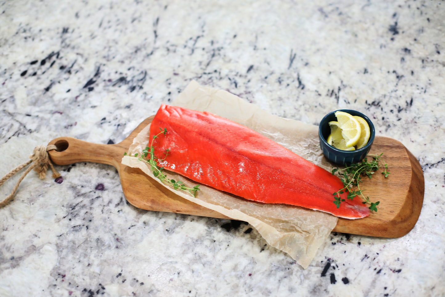 Fresh wild-caught Alaskan salmon fillet on wooden cutting board with lemon slices and herbs, premium sustainably harvested salmon from Bristol Bay, Net to Table Seafoods