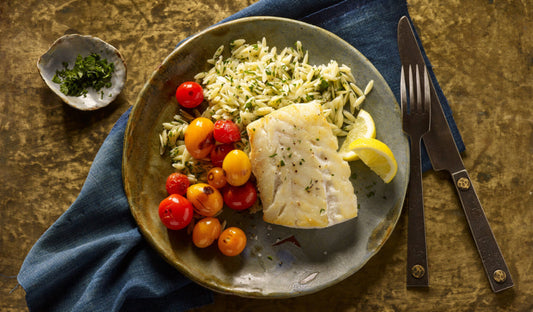Plate of white fish served with cherry tomatoes and rice, garnished with lemon wedges, on a rustic wooden table.