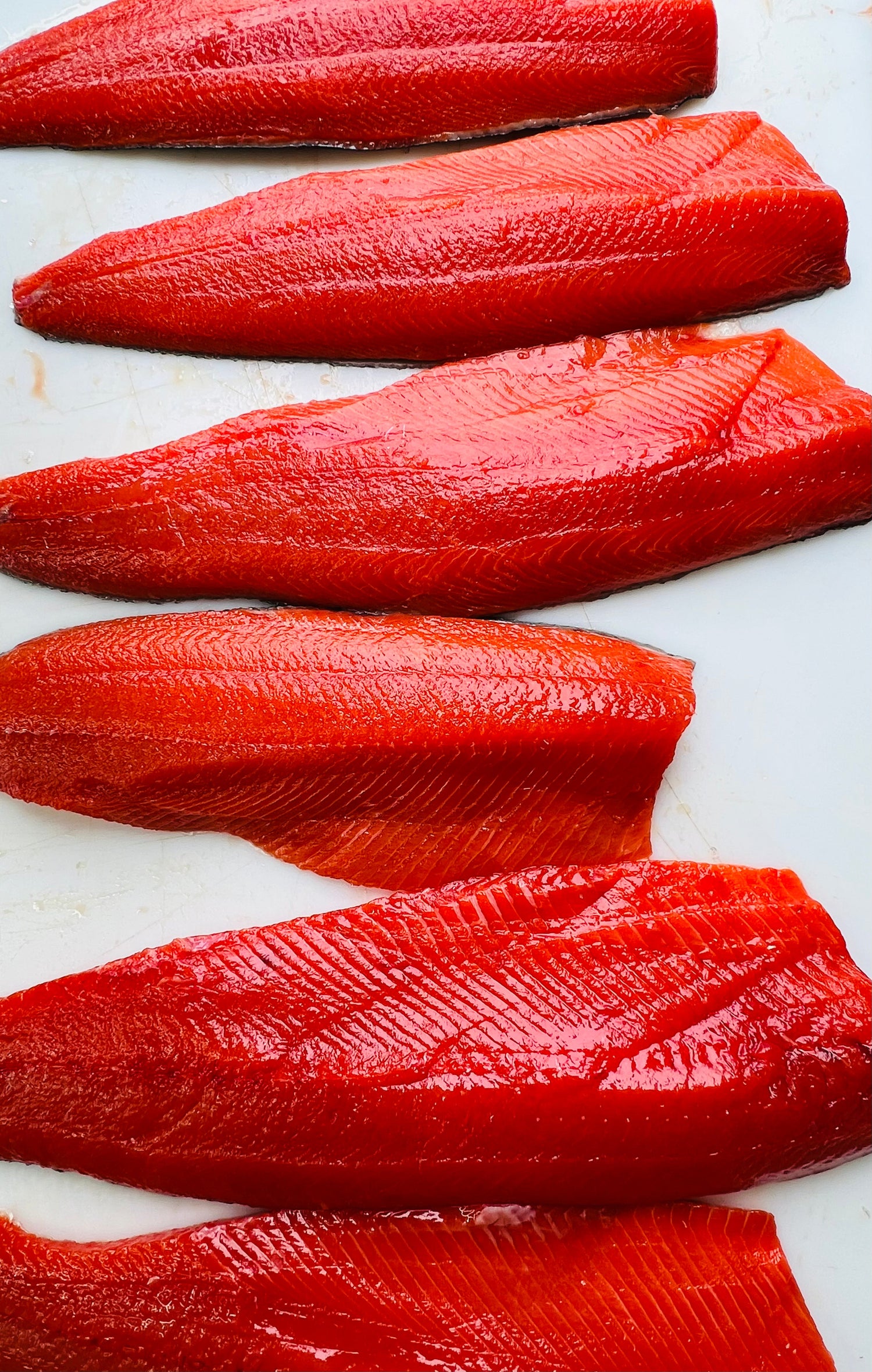Freshly filleted wild Alaskan sockeye salmon laid out in rows, showcasing their bright red color and clean cuts.