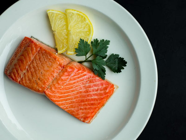 Cooked wild Alaskan salmon fillets served with lemon slices and parsley on a white plate – nutritious, omega-3 rich seafood.
