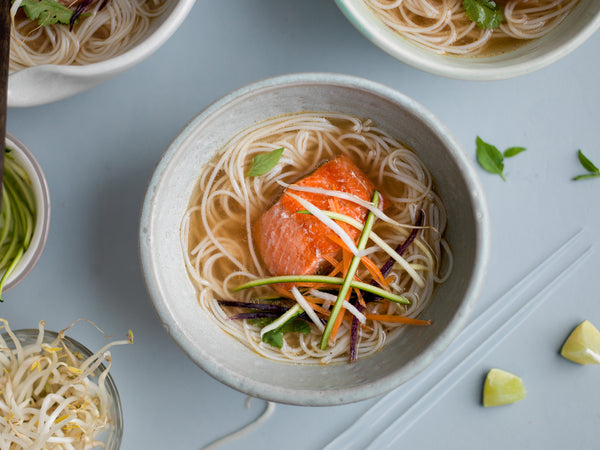 Wild-caught Alaskan salmon served in a bowl of noodle soup with fresh vegetables and herbs. A healthy and flavorful seafood dish made with sustainable salmon from Net to Table Seafoods.
