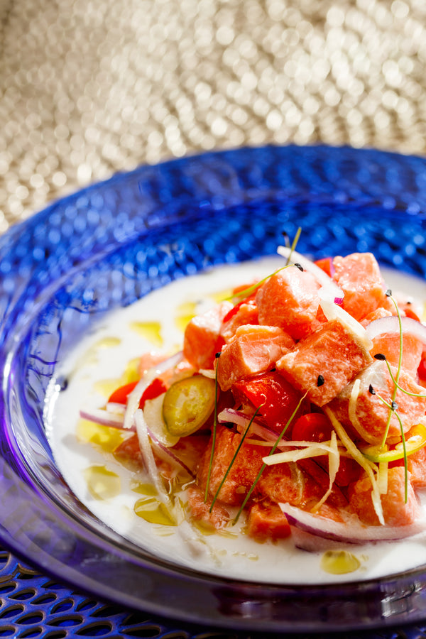 Wild-caught Alaskan salmon ceviche with fresh onions, peppers, and citrus served in a blue glass bowl. A vibrant, healthy seafood dish made with sustainable salmon from Net to Table Seafoods.
