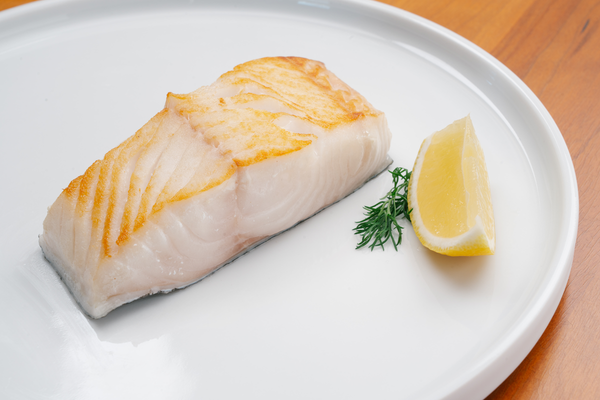Pan-seared wild Alaskan halibut fillet served with lemon and dill on a white plate. Fresh, flaky, and sustainably sourced from Alaska’s cold waters.
