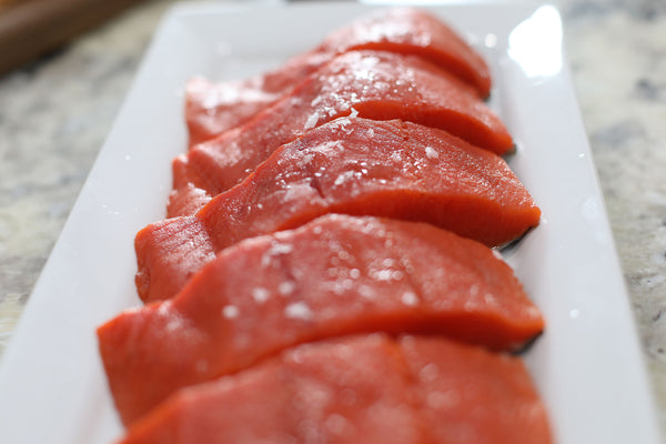 Close-up of fresh wild-caught Alaskan sockeye salmon fillets sprinkled with sea salt on a white serving plate – vibrant red flesh highlighting premium quality sustainable seafood.

