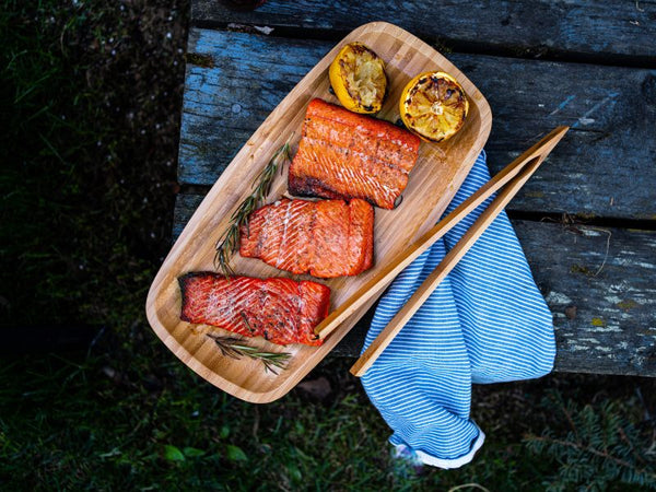 Grilled wild-caught Alaskan salmon fillets served on a wooden platter with charred lemons and fresh rosemary, highlighting rich color, smoky flavor, and sustainable seafood quality.
