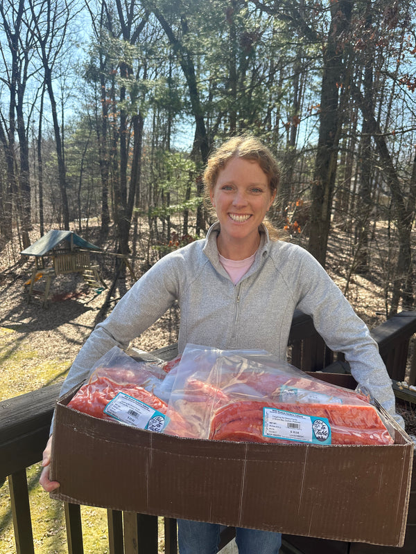 Smiling woman holding a box of vacuum-sealed wild-caught Alaskan salmon from Net to Table Seafoods, showcasing fresh sustainable fish delivered from Bristol Bay, Alaska. Family-owned small-boat fishery providing premium wild salmon direct to customers.
