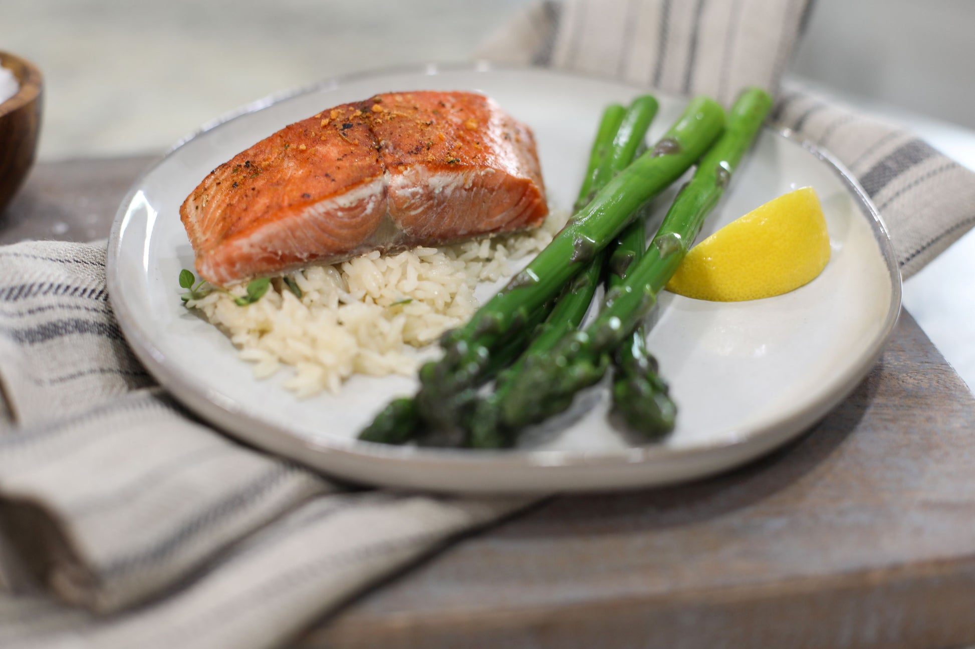 Cooked wild Alaskan salmon fillet with asparagus and rice on white plate with lemon wedge, Net to Table Seafoods healthy dinner meal on wooden table