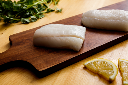 Fresh wild-caught Alaskan halibut fillets on wooden board with lemon slices and herbs, sustainably harvested whitefish from Net to Table Seafoods known for mild flavor and flaky texture