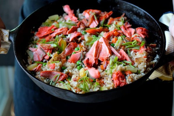 Cast-iron skillet filled with wild-caught Alaskan salmon fried rice, mixed with vegetables and green onions. A hearty, flavorful seafood dish made with sustainably sourced salmon.
