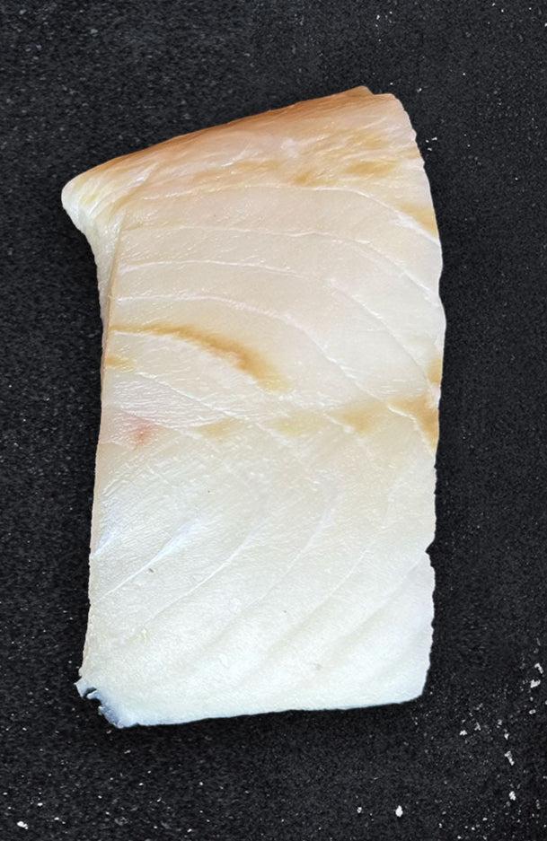 Raw wild Alaska halibut fillet on dark background, displaying pristine white flesh and firm texture of premium whitefish portion