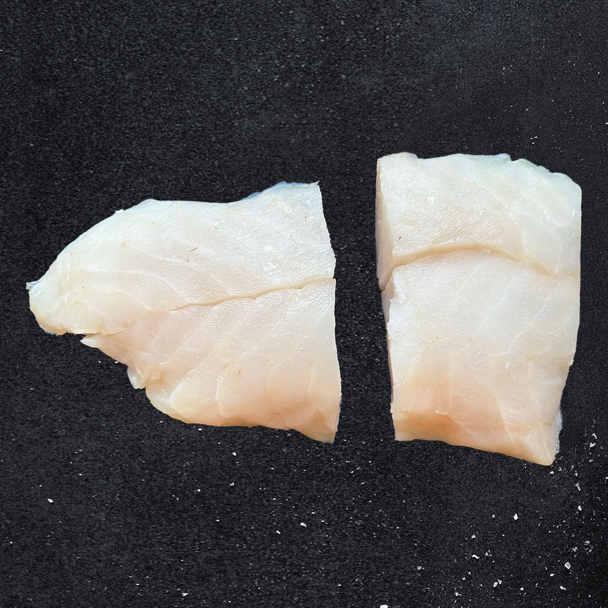Two portions of wild-caught Alaskan black cod fillet on a dark background, highlighting the fish’s firm texture and natural sheen. Premium sablefish sustainably harvested from Alaska.
