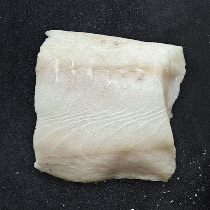 Close-up of a raw fillet of wild-caught Alaskan black cod (sablefish) on a dark background, showcasing its buttery texture and delicate white flesh—premium seafood from Net to Table Seafoods.
