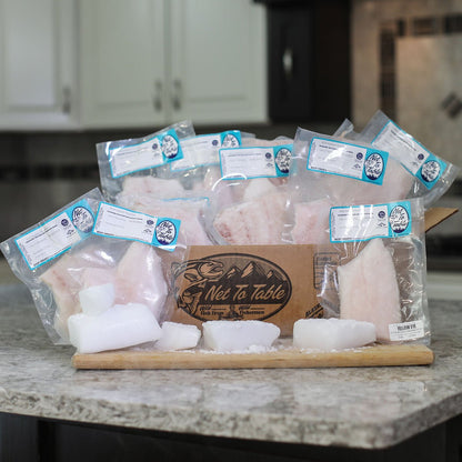 Wild Alaska whitefish gift box with 12 vacuum-sealed portions arranged on wooden board, featuring Net to Table branded packaging in kitchen setting