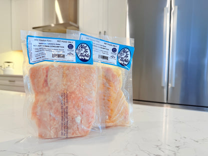 Two packages of frozen wild Alaskan Keta salmon pet food from Net to Table Seafoods on kitchen counter with refrigerator