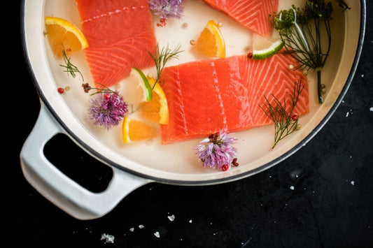 Raw wild-caught King Salmon fillet from Bristol Bay, Alaska displayed on white ceramic dish with fresh herb sprigs and orange slice garnish against dark background